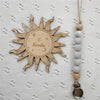 A wooden sun-shaped bead pacifier clip with a silicone teether is displayed on a white textured fabric.
