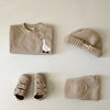A beige baby long sleeve cartoon top and pants set with a matching knit beanie and soft fabric item.