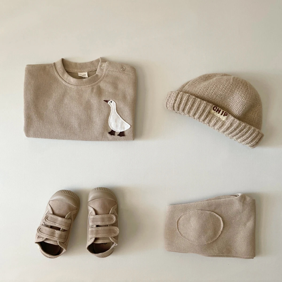 A beige baby long sleeve cartoon top and pants set with a matching knit beanie and soft fabric item.