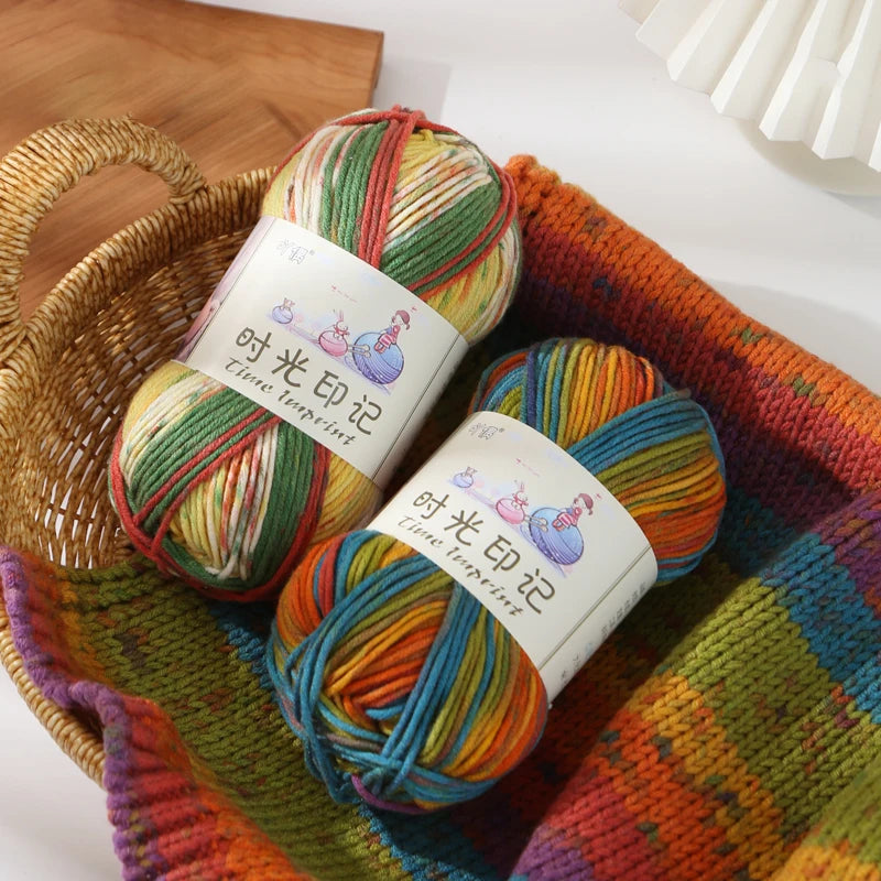A bundle of three skeins of gradient acrylic yarn in various colors resting in a woven basket and an orange knitted fabric.