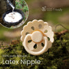 A light beige latex nipple pacifier resting on green moss with a dripping liquid in the background.