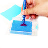 A hand holds a blue diamond painting tool over a clear storage tray filled with blue beads.