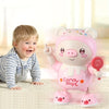 A smiling baby is interacting with a pink, interactive pig toy that lights up and plays music.