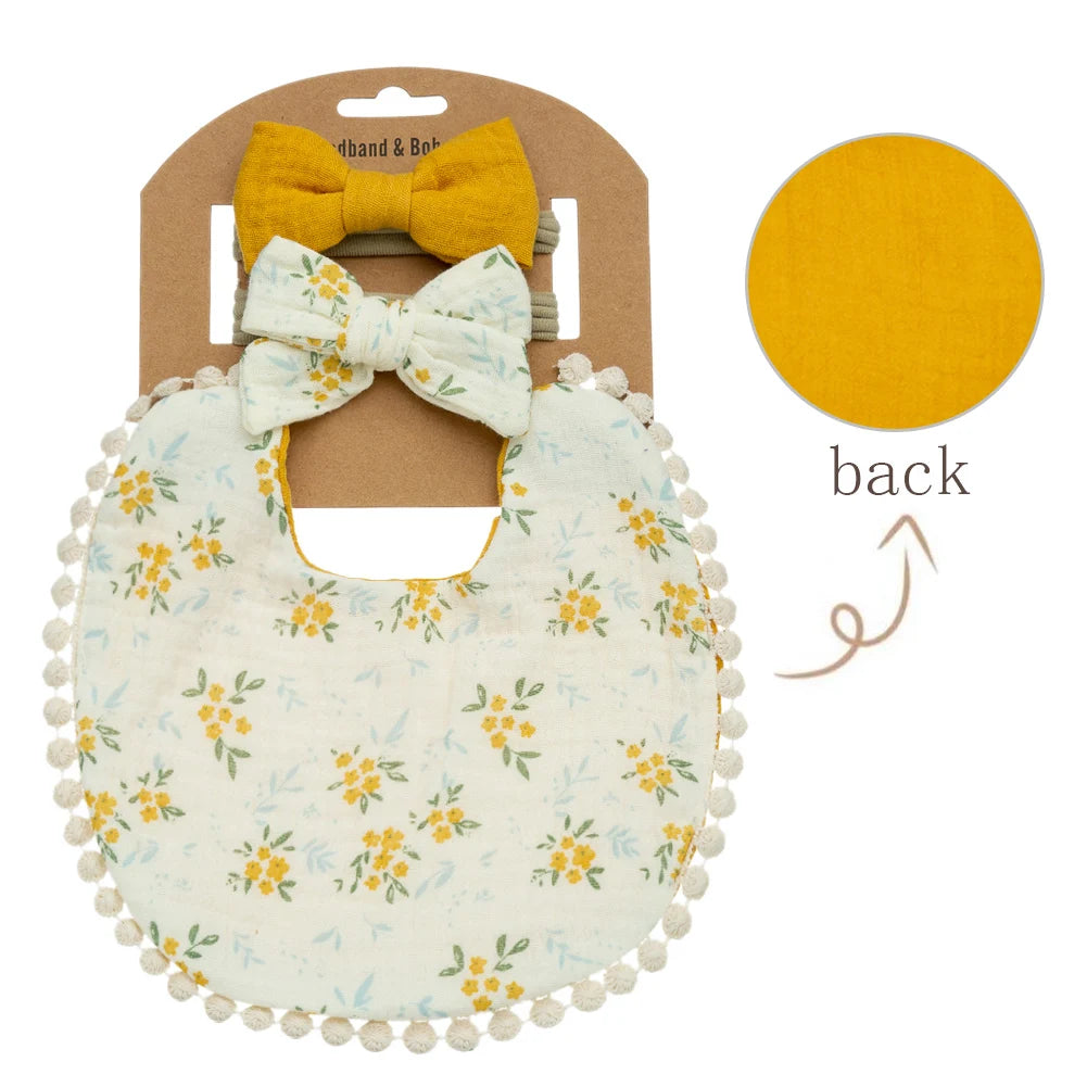 A light yellow floral baby bib and matching bow headband set displayed in a cardboard packaging.