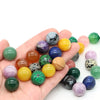 A hand holds various natural amethyst and rose quartz crystal spheres of different colors.