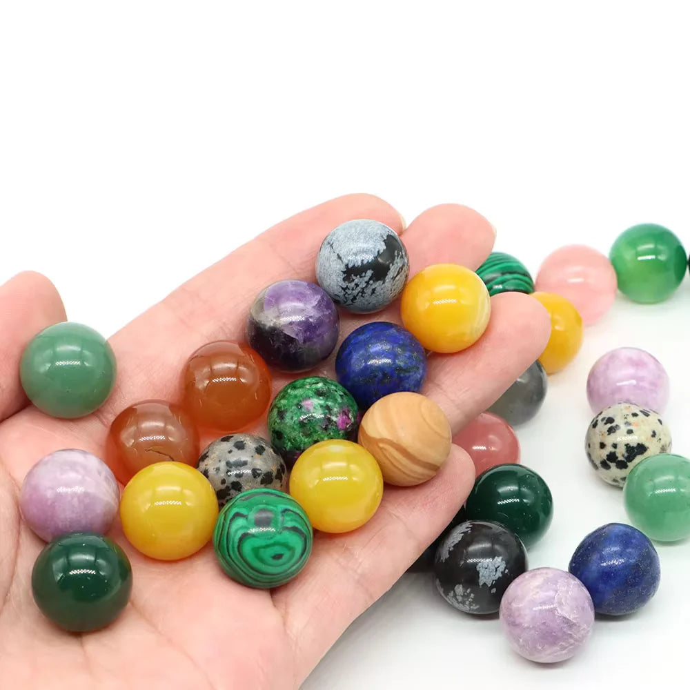 A hand holds various natural amethyst and rose quartz crystal spheres of different colors.