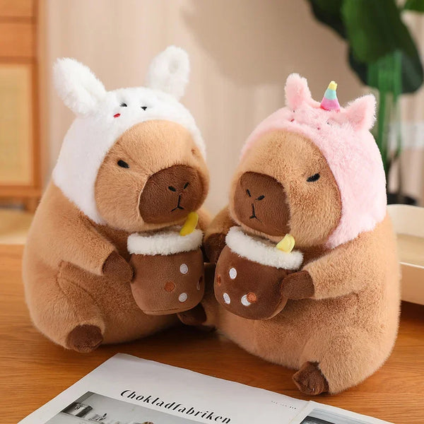A pair of brown capybara plush toys wearing pink and white outfits sitting on a wooden surface.