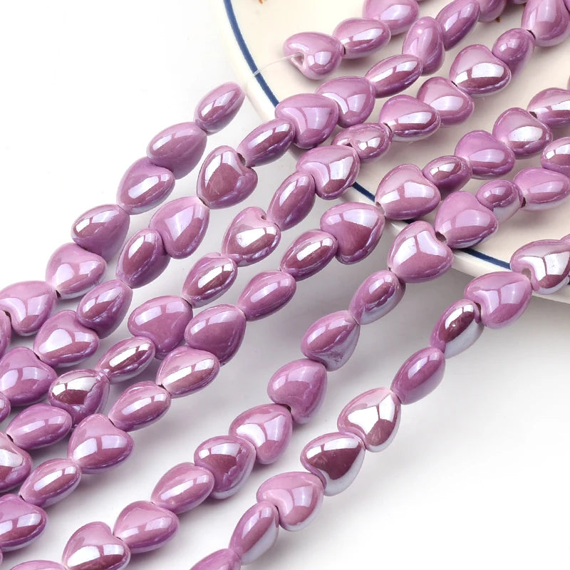 A string of purple heart-shaped acrylic beads for jewelry making laid out on a white background.