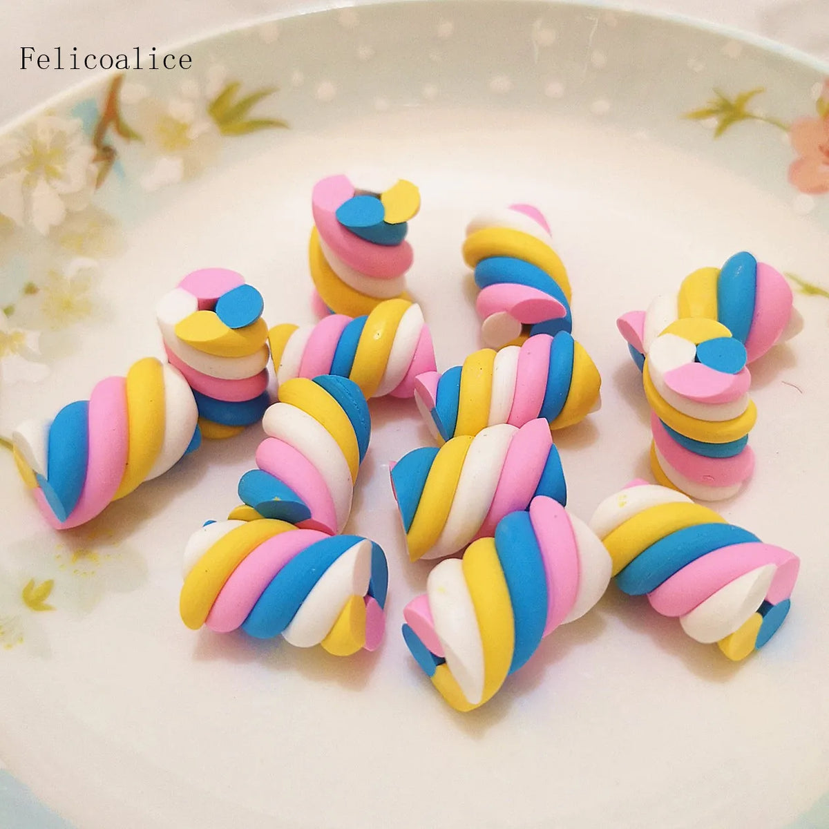 A collection of colorful polymer clay marshmallow charms in striped designs arranged on a white plate.
