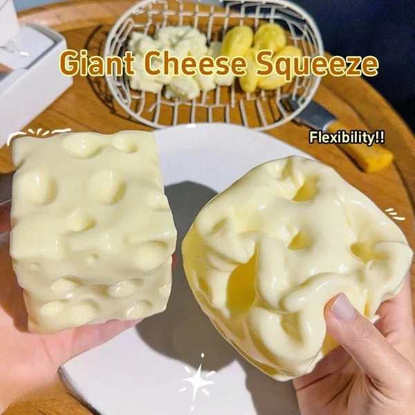 A hand holds a large, yellow, moldable cheese-shaped squishy toy on a white plate.