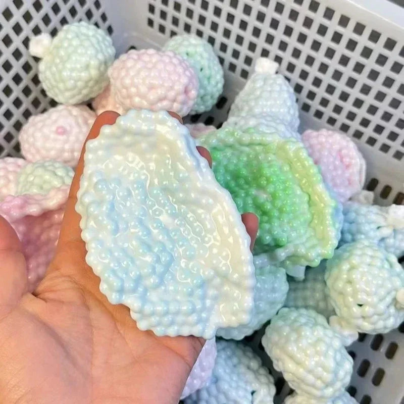 A hand holds a light blue squishy stress relief ball surrounded by various pastel-colored squishy balls in a white basket.