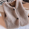 A beige, fuzzy lamb wool vest for children is displayed on a light-colored woven surface.
