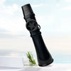 A black portable kazoo flute with a lanyard is shown against a light blue sky and water, resting on a white surface.