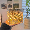 A clear cube night light filled with glowing yellow and orange tulip-shaped lights, held in a person's hand.