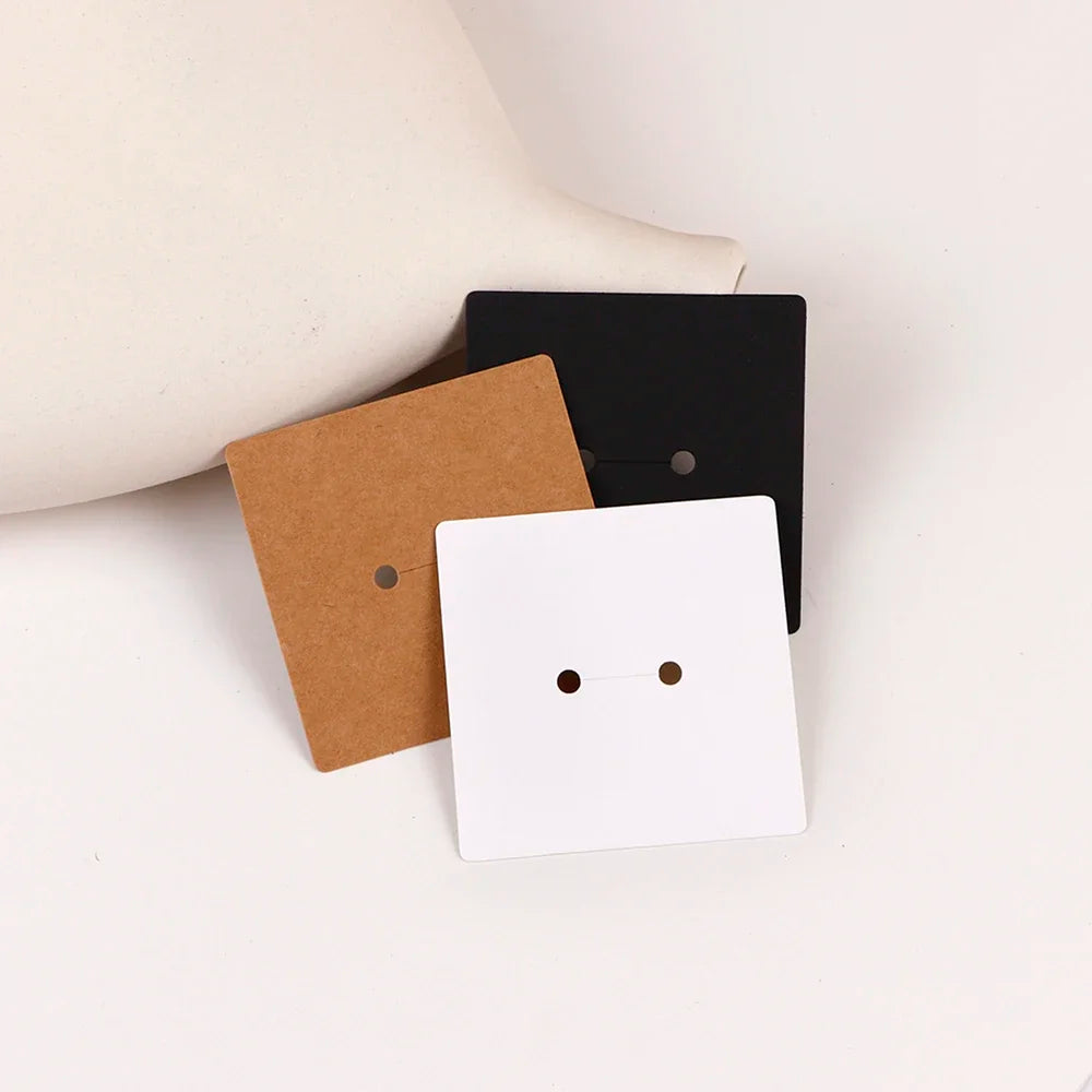 Three square jewelry display cards in kraft brown, black, and white are shown on a white background.