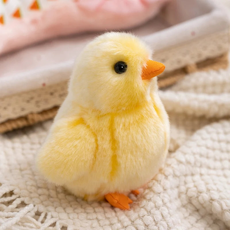 A fluffy yellow chick plush toy with an orange beak resting on a light fabric surface.