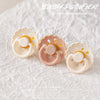 Three natural latex baby pacifiers in white and pink tones are displayed on a white textured background.