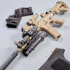 A tan electric gel blaster gun with a black stock and battery is shown next to a pair of tactical gloves.