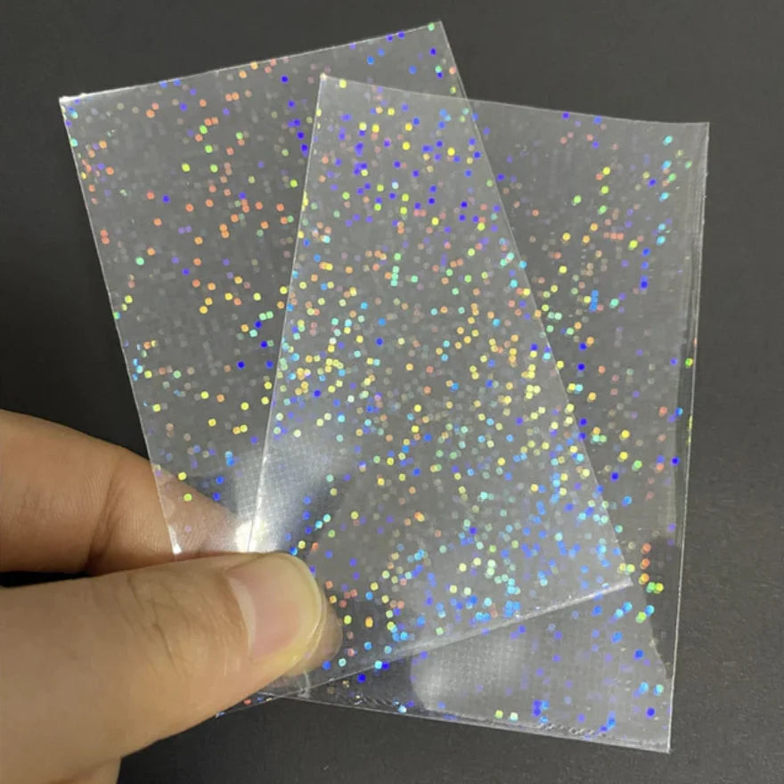 A hand holds a pack of holographic card sleeves with multicolored glitter particles.