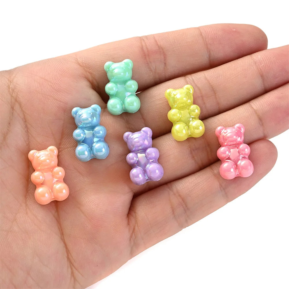 A hand holds several pastel colored bear-shaped acrylic craft beads.