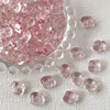 Pink geometric glass beads in irregular square shapes scattered on a white surface.