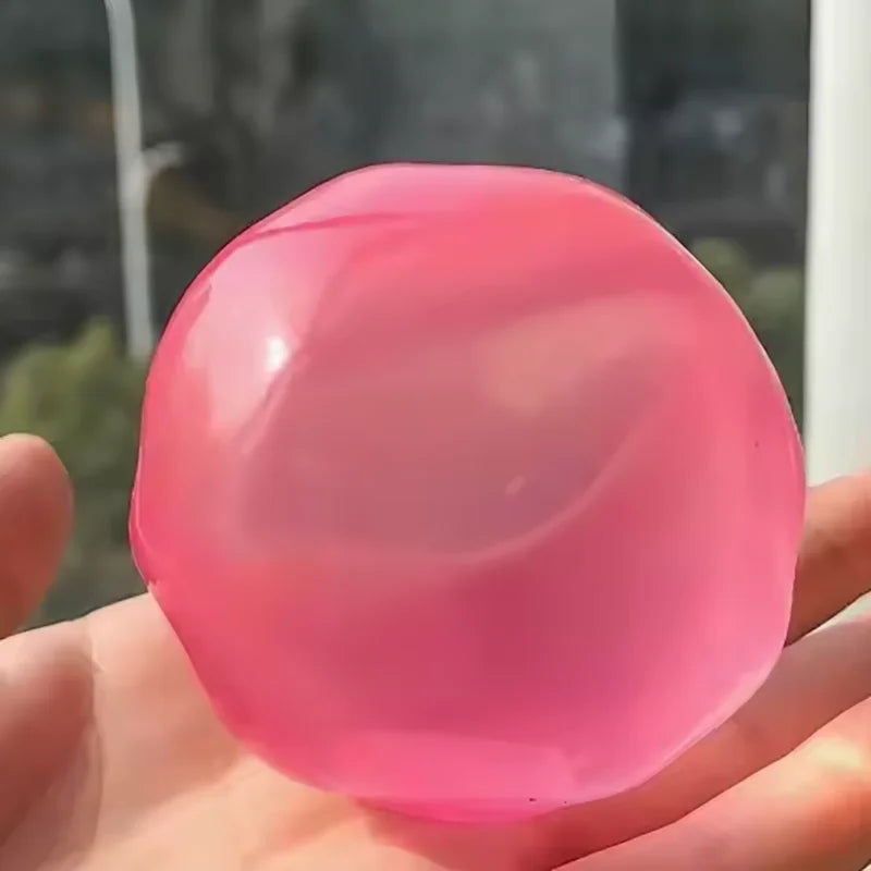 A close-up shot of a smooth, translucent pink squeezy fidget ball held in a person's hand.