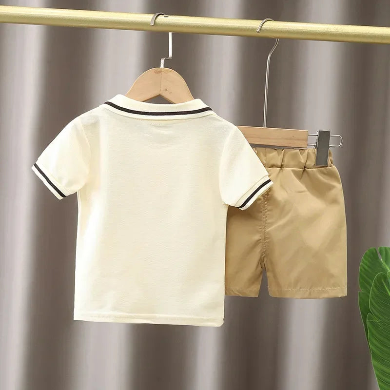 A beige boys' cotton summer short sleeve t-shirt and shorts set hanging on a wooden hanger.