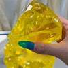 A hand holds a translucent yellow honey cheese squishy stress ball with a green fingernail.