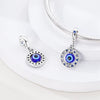 A pair of sterling silver charm beads featuring cross, angel, and evil eye designs displayed on a white surface.