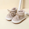 A pair of beige baby winter snow boots with plush lining and rubber soles resting on a light surface.