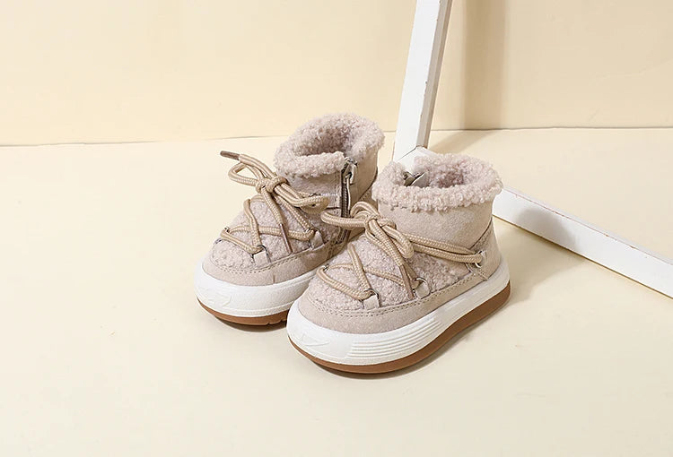 A pair of beige baby winter snow boots with plush lining and rubber soles resting on a light surface.