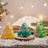 A set of festive silicone Christmas tree cookie and candle molds with a lit candle on a wooden slice surrounded by artificial