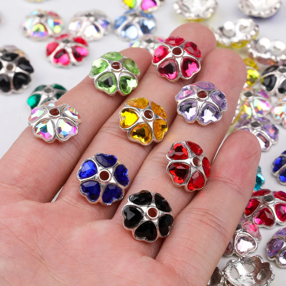A hand holds various heart-shaped rhinestone flower charm beads in multiple colors and sizes.