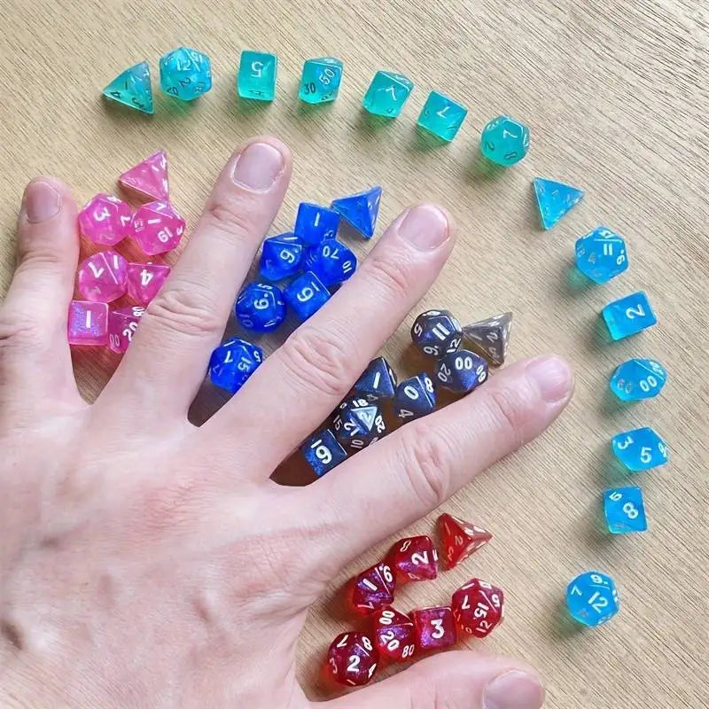 A hand holds a collection of iridescent acrylic polyhedral dice in various colors and sizes on a wooden surface.