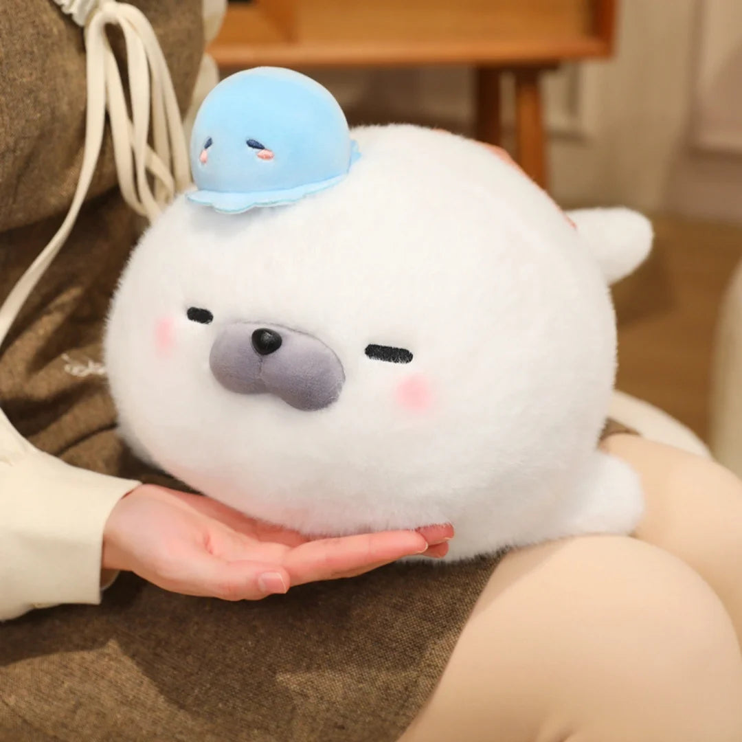 A white seal plush toy with a light blue octopus hat being held in a person's hand.
