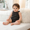 A baby wearing a dark gray denim romper sitting on a white couch.