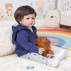 A baby doll with soft cloth body wearing a blue hoodie and patterned pants sitting on a fluffy white rug.