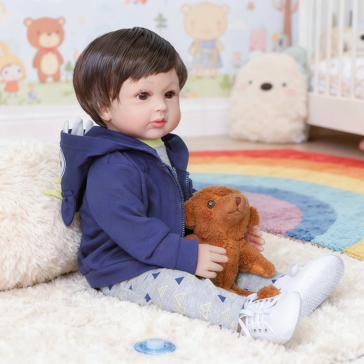 A baby doll with soft cloth body wearing a blue hoodie and patterned pants sitting on a fluffy white rug.