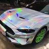A silver sports car features a holographic chrome vinyl wrap with a rainbow finish on its hood and body.