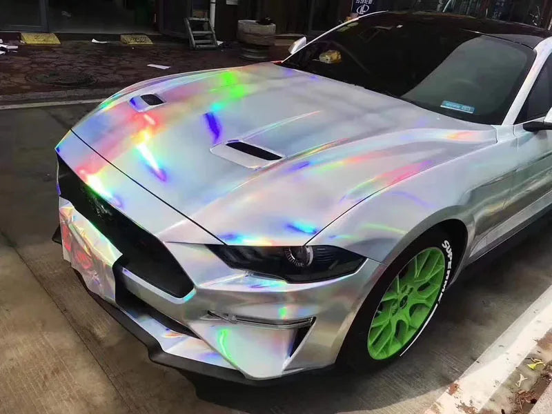 A silver sports car features a holographic chrome vinyl wrap with a rainbow finish on its hood and body.
