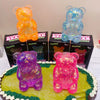 A collection of slow-rising glitter bear squishy toys in orange, blue, and pink are displayed on a green surface.