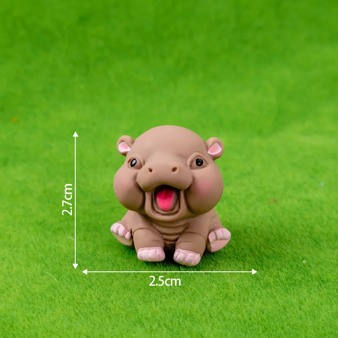 A small, light brown resin figurine of a happy hippo in a sitting pose, photographed on green grass.