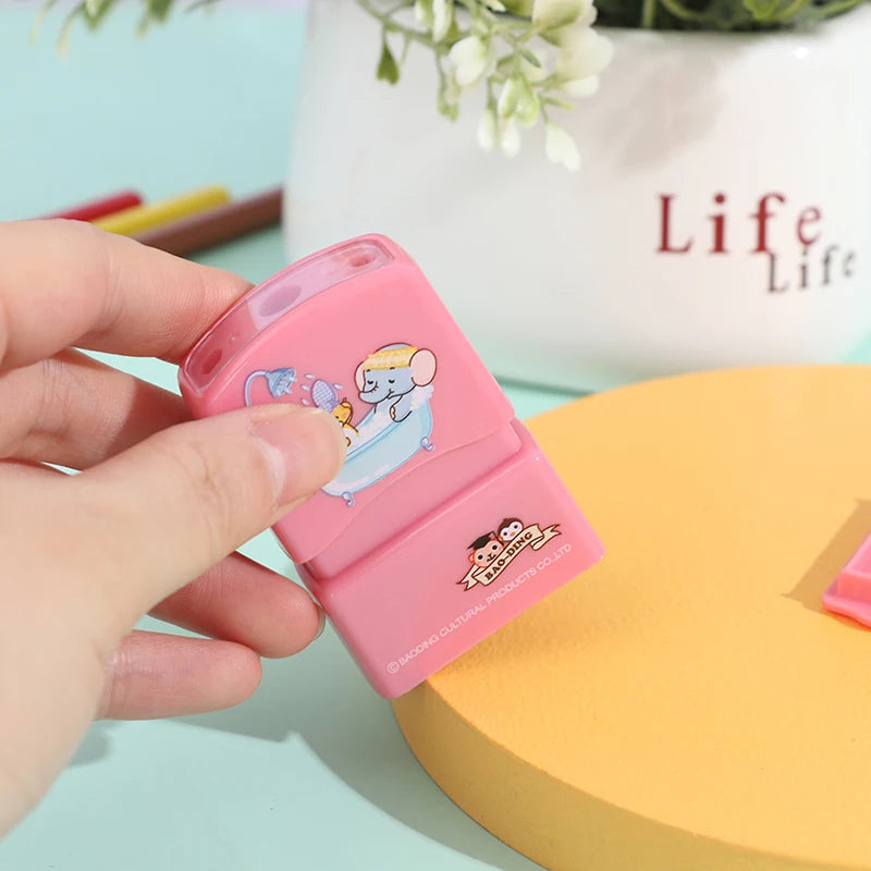A hand holds a pink custom kids name stamp with a light blue design against a yellow background.