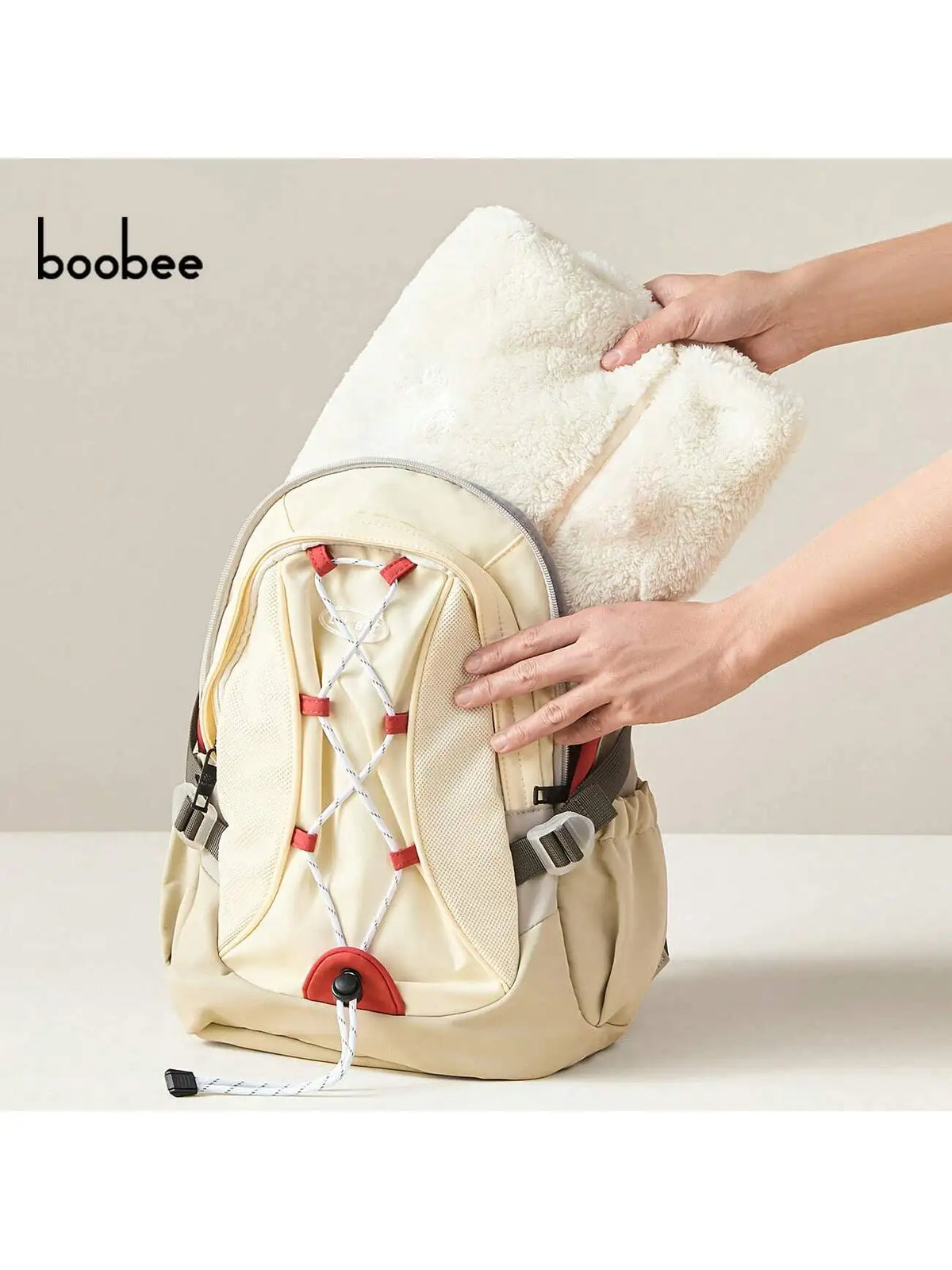 A beige baby windproof cape blanket with a white fluffy trim and dinosaur design is being held by a hand.