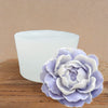 A light purple silicone flower mold rests on a wooden surface next to a white, translucent object.