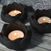 Three black lotus flower silicone molds holding glowing candles on a wooden surface.