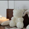 A white silicone mold shaped like a fluffy bear is shown next to a lit candle.