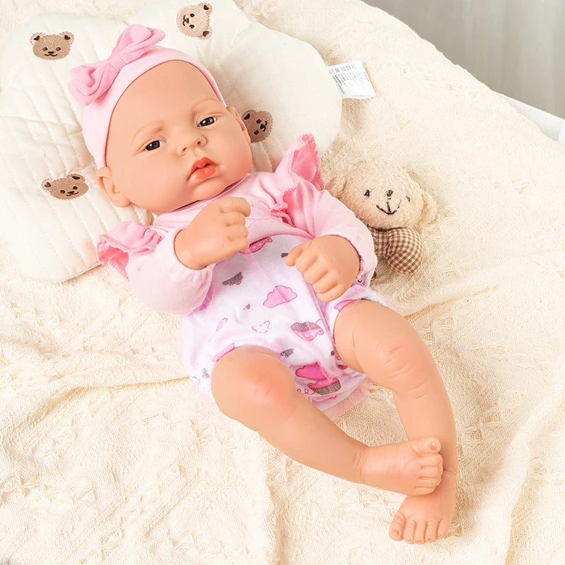 A lifelike vinyl reborn doll with a pink outfit and bow lying on a cream blanket.