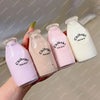Three pink and white squishy milk bottles are held by a hand against a light background.