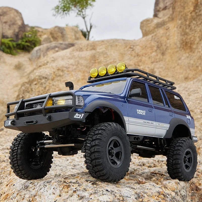 A blue 1:18 scale remote control off-road climbing jeep with a black roof rack parked on rocks.